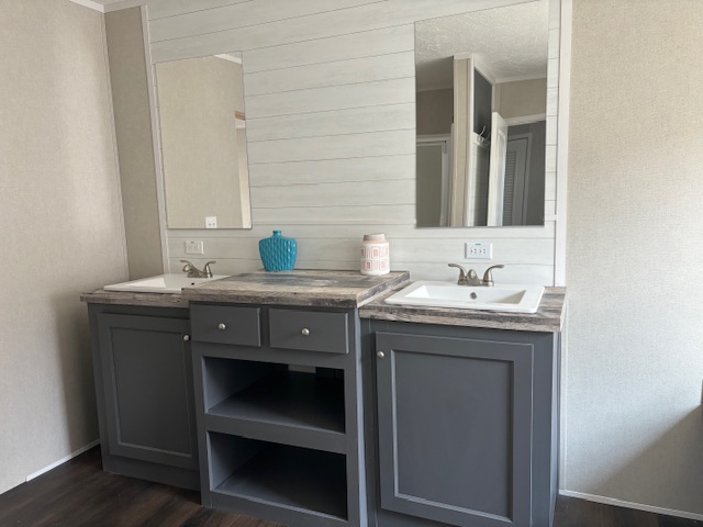 Gray dual-sink bathroom vanity with white sinks, marble countertop, and two mirrors. A blue vase and patterned jar add color. Elegant and modern.