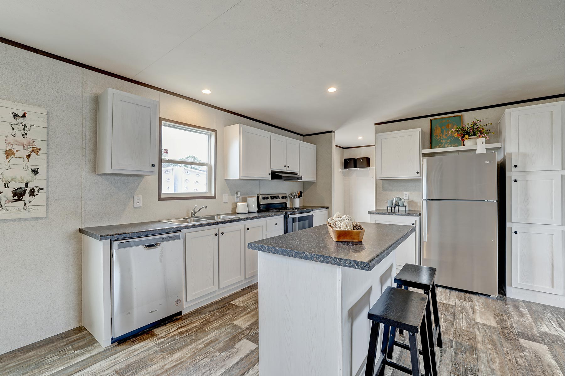 Bright, modern kitchen with white cabinets, stainless steel appliances, and wood-look flooring. An island with black stools adds contrast. Cozy and inviting.