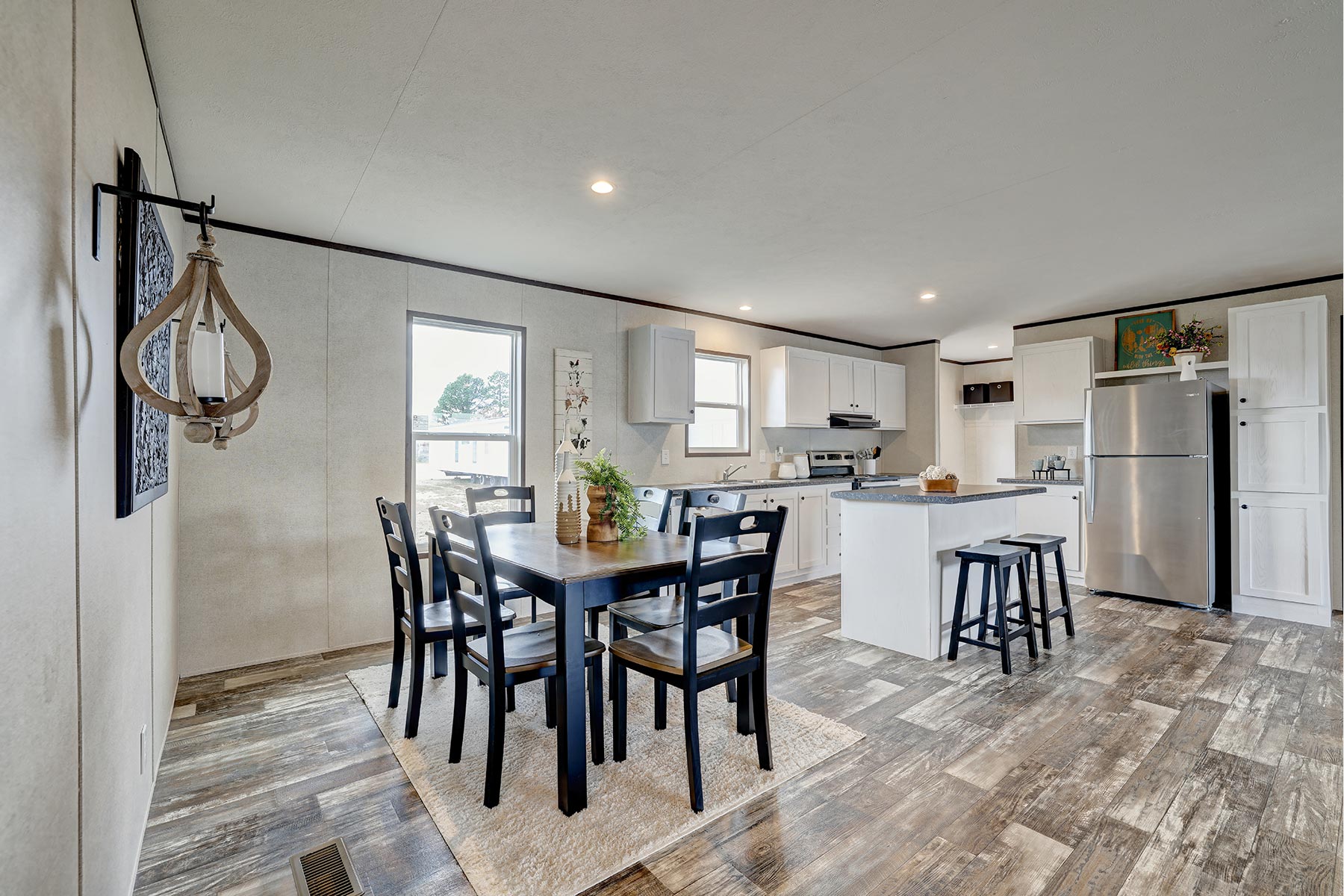 Modern kitchen and dining area with a wooden floor. Features a dark dining table, black chairs, white cabinetry, island with stools, and stainless steel appliances. Cozy and inviting ambiance.