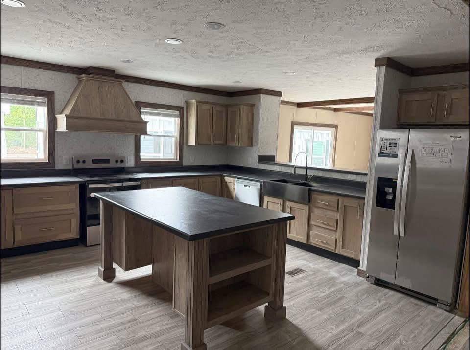 Modern kitchen featuring wooden cabinets, stainless steel appliances, and a central island. Sunlight streams through windows, creating a warm, inviting atmosphere.