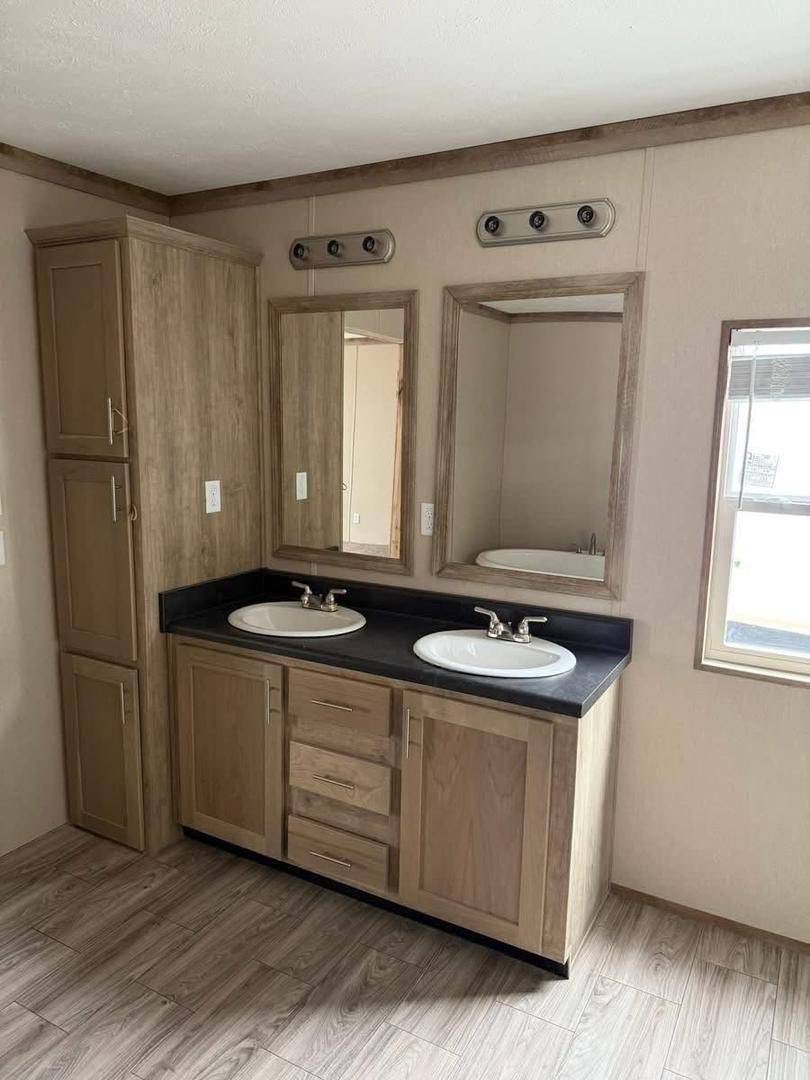 A bathroom with wooden cabinets, dual sinks, and large mirrors on a light wall. Light wood flooring adds a warm, inviting tone.