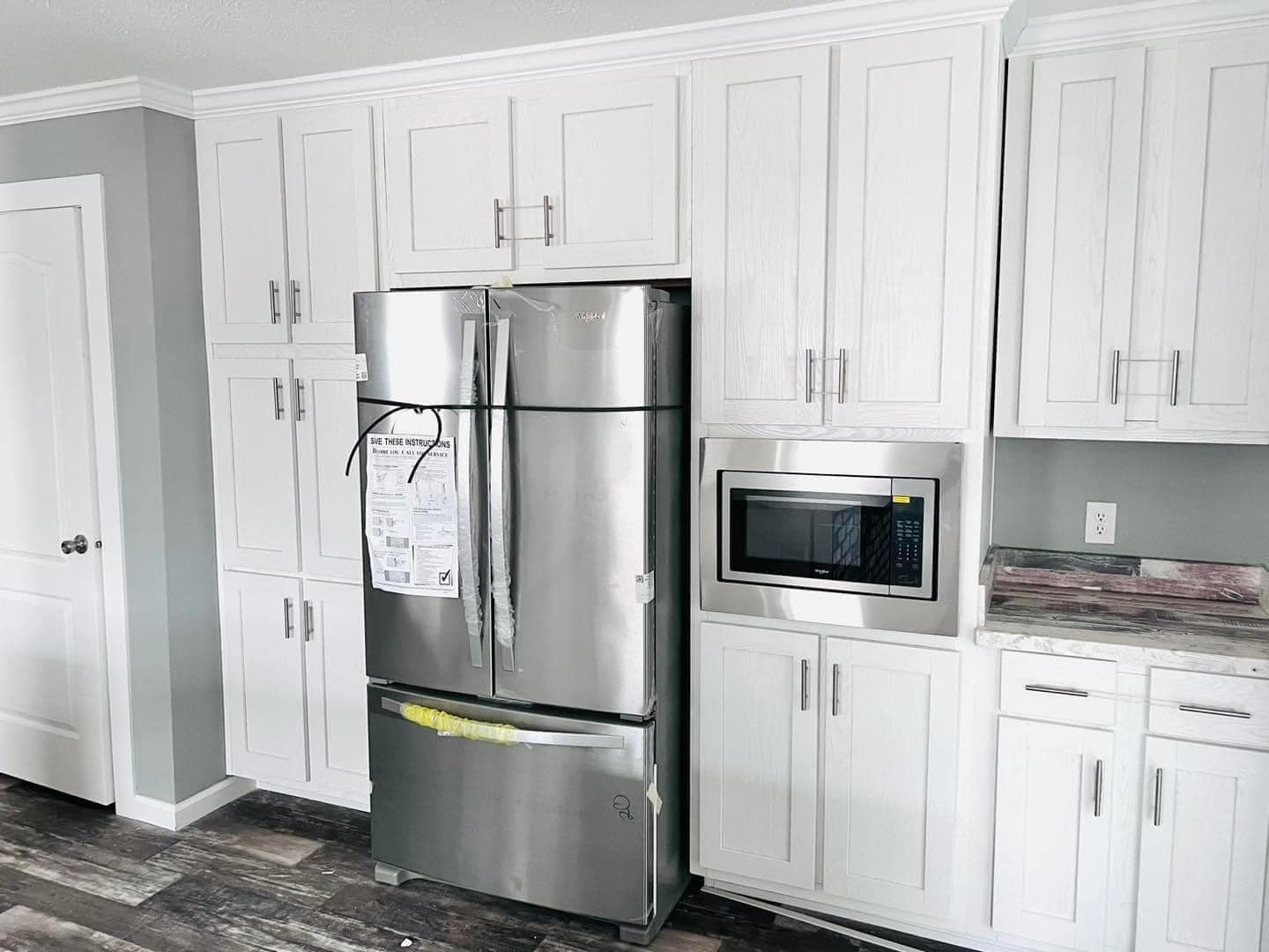Modern kitchen with white cabinets and a sleek stainless steel refrigerator. A built-in microwave sits beside it, creating a clean, contemporary look.