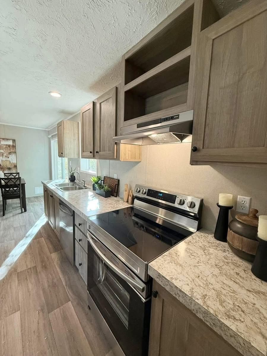 Modern kitchen with light wood cabinets, marble countertops, and stainless steel appliances. Bright sunlight streams through a window, creating a welcoming atmosphere.
