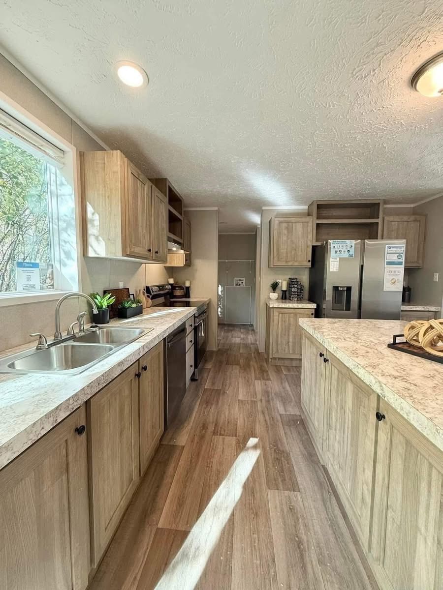 Bright kitchen with light wood cabinets, marble countertops, and stainless steel appliances. Sunlight streams through a large window, creating a cozy and inviting atmosphere.
