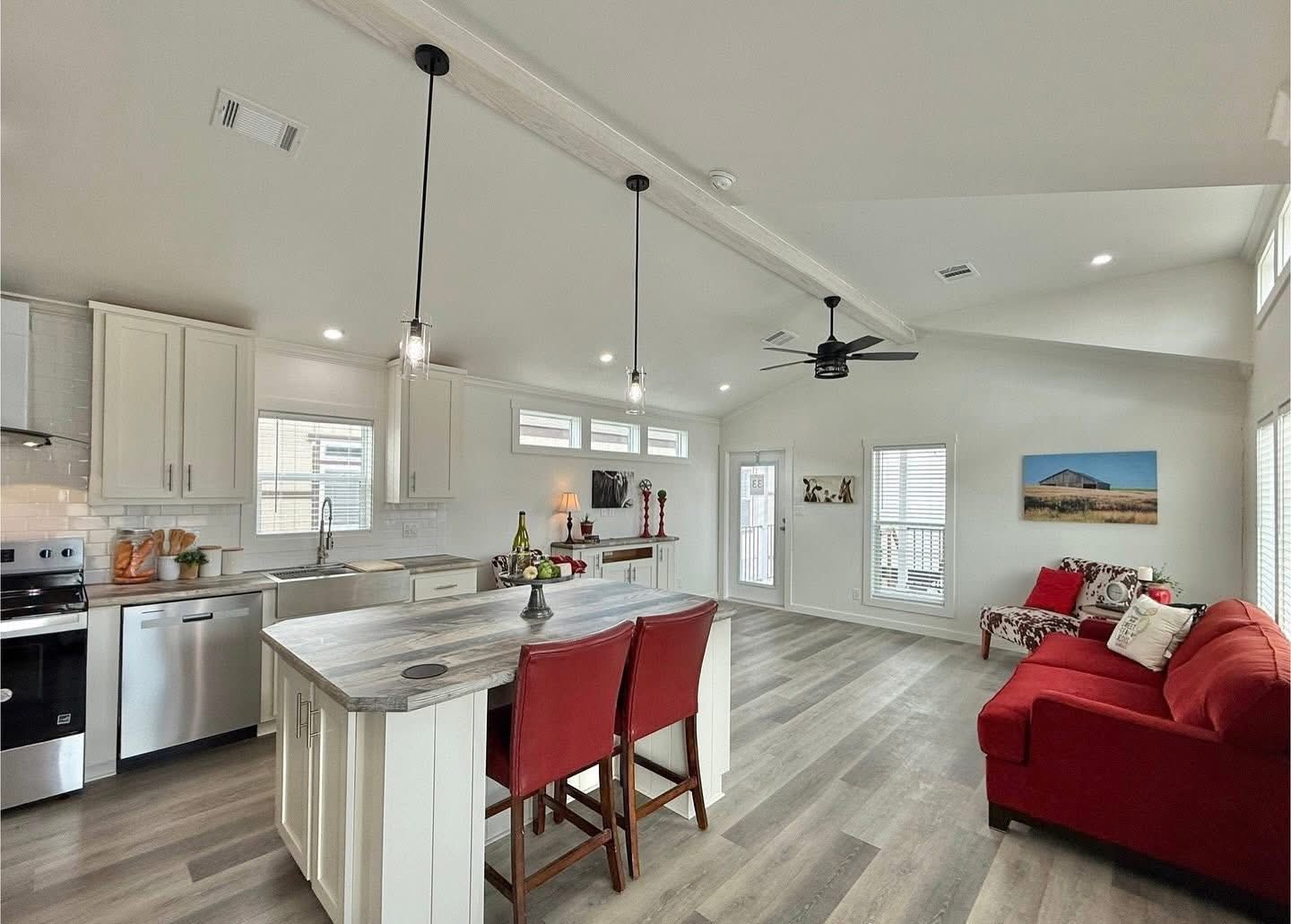Spacious, modern kitchen and living room with white cabinets, stainless appliances, and a large island. Red chairs and sofa add warmth and contrast.