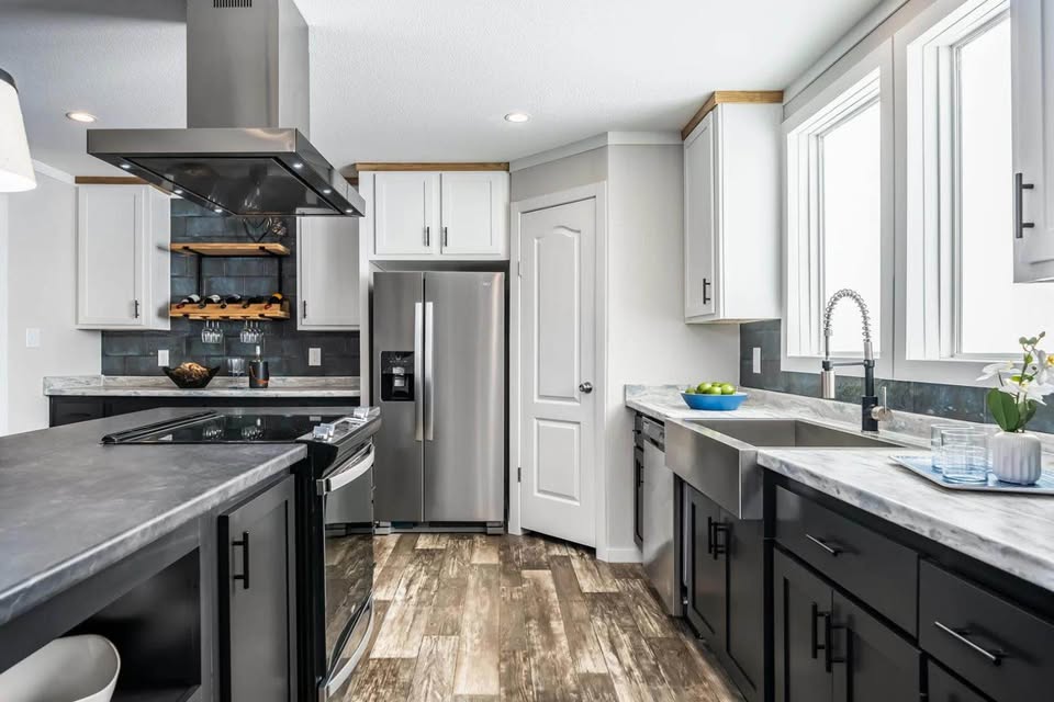 Modern kitchen with stainless steel appliances, white and dark cabinets, grey countertops, and wood-style flooring. Bright and clean ambiance.