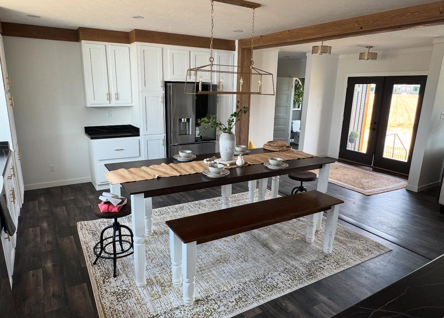 A modern kitchen with dark wood floors and white cabinets, featuring a central island with plants and tableware. Warm, inviting atmosphere with natural light.