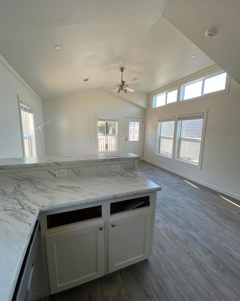 Bright, modern room with high ceiling features large windows, marble countertop, and light wood flooring. Ceiling fan adds elegance and airiness.