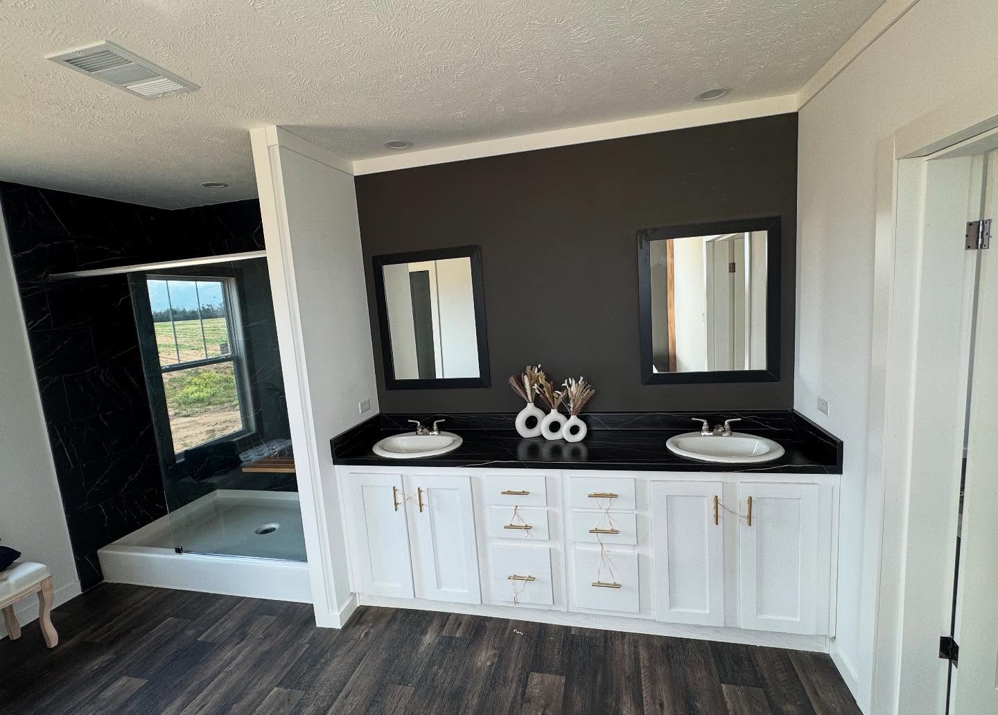 Modern bathroom with dual sinks on a black countertop, white cabinets, and two mirrors. Dark accent wall and shower area with a glass enclosure.