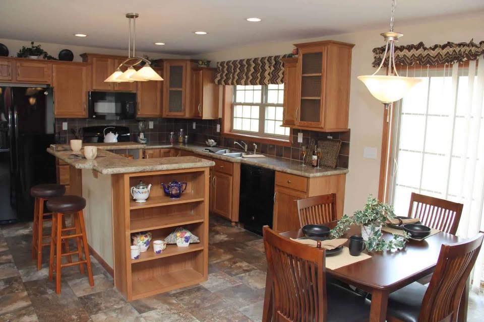 Cozy kitchen with wooden cabinets, granite countertops, and an island with stools. Dining table set for four. Warm lighting and patterned curtains.