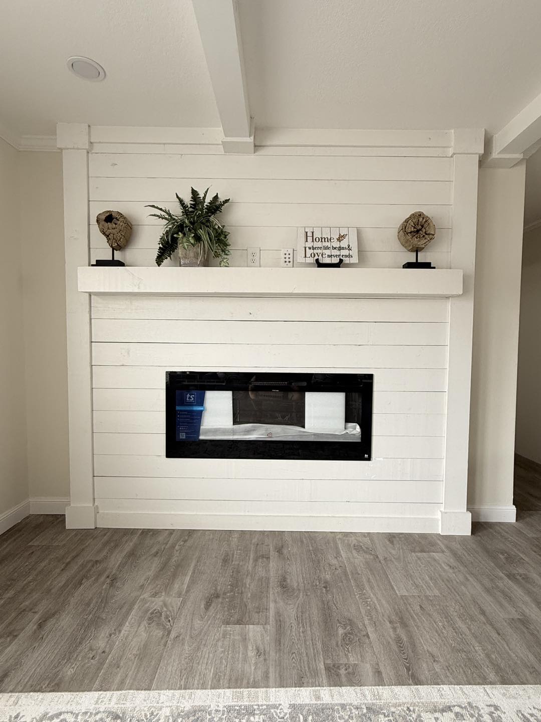 Modern fireplace set in white shiplap wall, featuring decorative globes and a plant on the mantel. Light wood flooring adds a cozy, minimalist vibe.