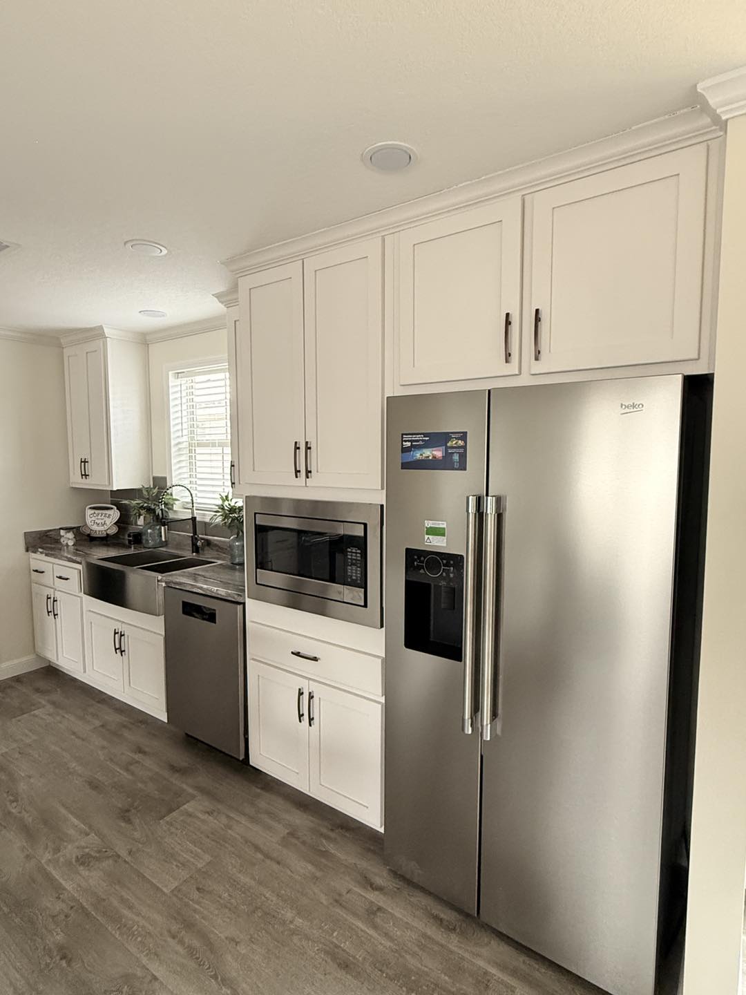 Modern kitchen with light wood cabinets, stainless steel appliances, and wood flooring. Includes a double sink, dishwasher, microwave, and large fridge.
