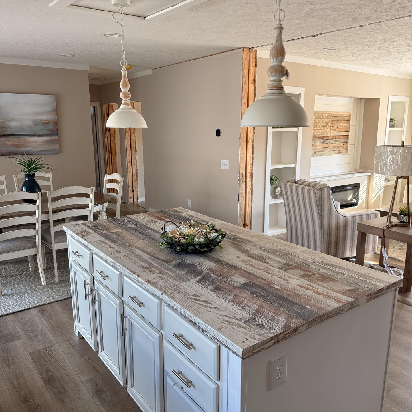 Cozy kitchen with a rustic island featuring a wooden countertop and white cabinets. Nearby, a dining area with chairs, pendant lights, and soft tones.