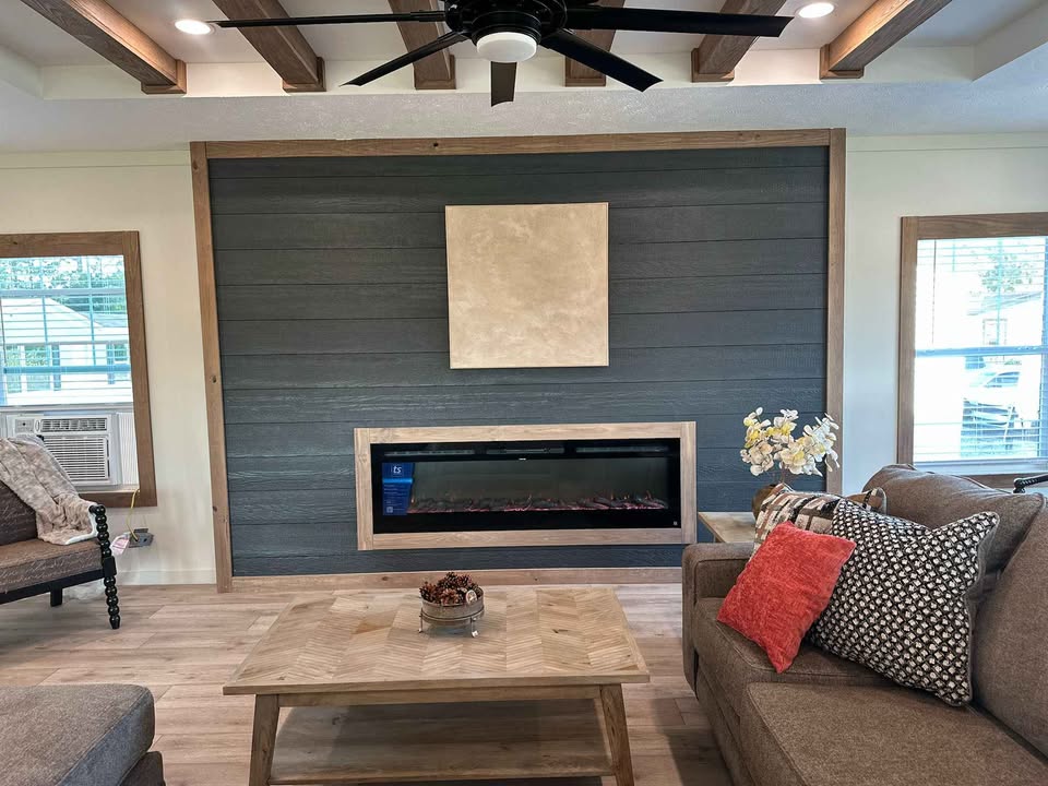 Cozy living room with dark wood accent wall, modern fireplace, beige artwork, and brown sofa. Bright throw pillows add a pop of color. Warm, inviting atmosphere.