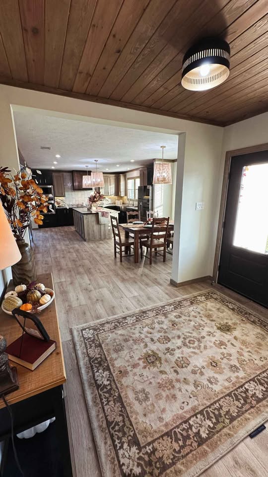 Warm, cozy home interior featuring a wood ceiling and floor, a patterned rug, and an inviting dining area with rustic accents and autumn decor.
