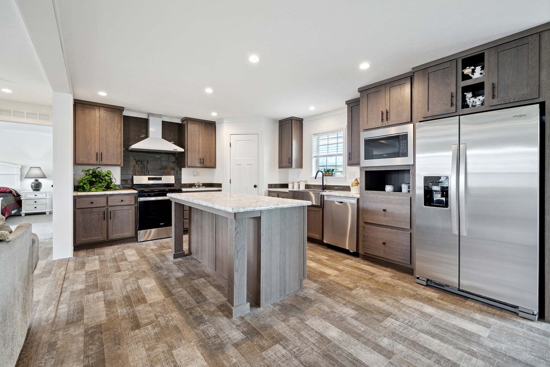 Modern kitchen with stainless steel appliances, dark wood cabinets, and a central island with a marble countertop. Bright and spacious ambiance.