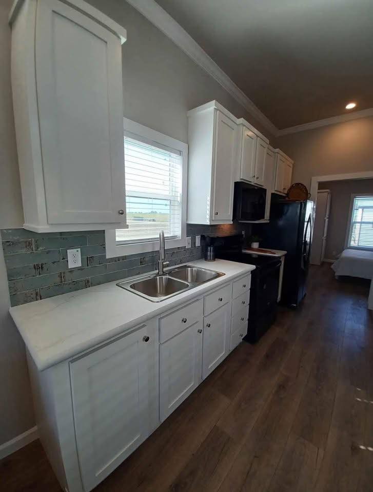 Bright kitchen with white cabinets, a dual sink, and a green tile backsplash. Wood flooring adds warmth. Appliances and window add a modern touch.