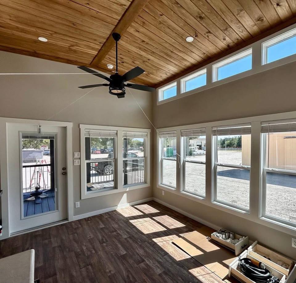 Bright room with large windows, wooden ceiling, and fan. Sunlight casts shadows on the wooden floor, creating an inviting, airy atmosphere.