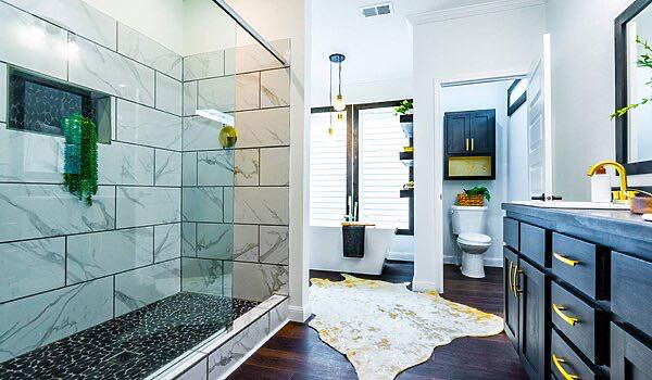 Modern bathroom with a glass-enclosed shower featuring marble tiles. Dark wood vanity, gold fixtures, toilet, and white tub on a cowhide rug. Bright, sleek ambiance.
