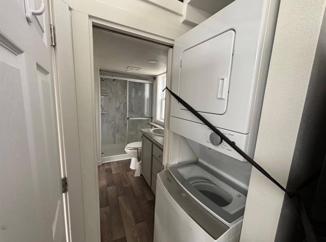 Compact space with a stacked washer-dryer and adjacent bathroom featuring a glass-enclosed shower, sink, and toilet; modern and efficient design.