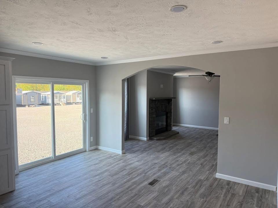 Modern living room with light gray walls, wood flooring, and sliding glass doors leading outside. An archway reveals a cozy fireplace. Bright and spacious.