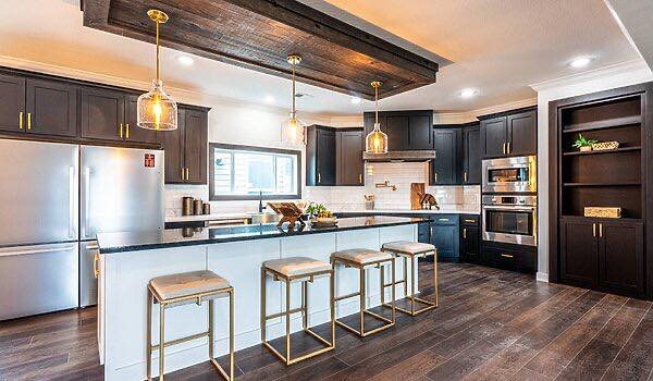 Modern kitchen with dark cabinets, stainless steel appliances, and a large island with white countertops. Pendant lights hang above, creating a warm, inviting atmosphere.