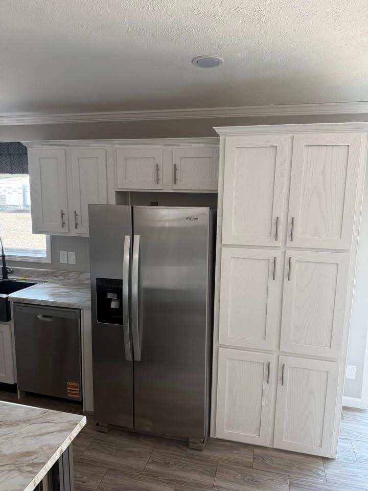 Modern kitchen with light wood cabinets, stainless steel fridge and dishwasher, and marble countertops. The space is clean, bright, and organized.