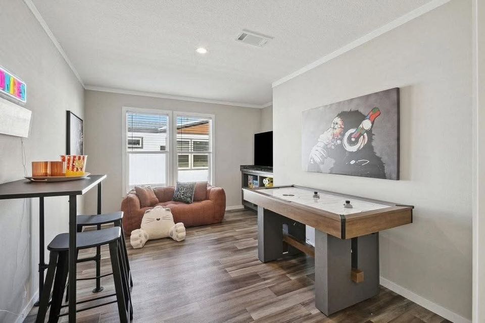 A modern game room with a brown air hockey table and a colorful gorilla painting on the wall. A cozy sofa and pillows are beneath a bright window.
