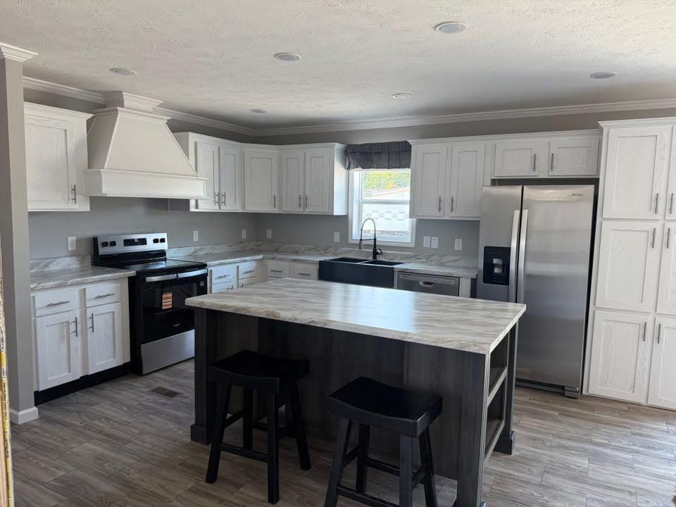 Modern kitchen with white cabinets, stainless steel appliances, and marble countertops. Center island features two black stools, creating a bright, sleek ambiance.