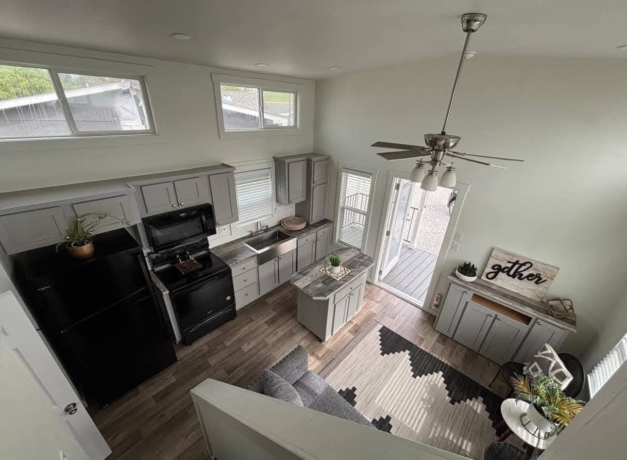 Modern kitchen view from above with gray cabinets, black appliances, island with greenery, and a “gather” sign. Bright, open, inviting space.