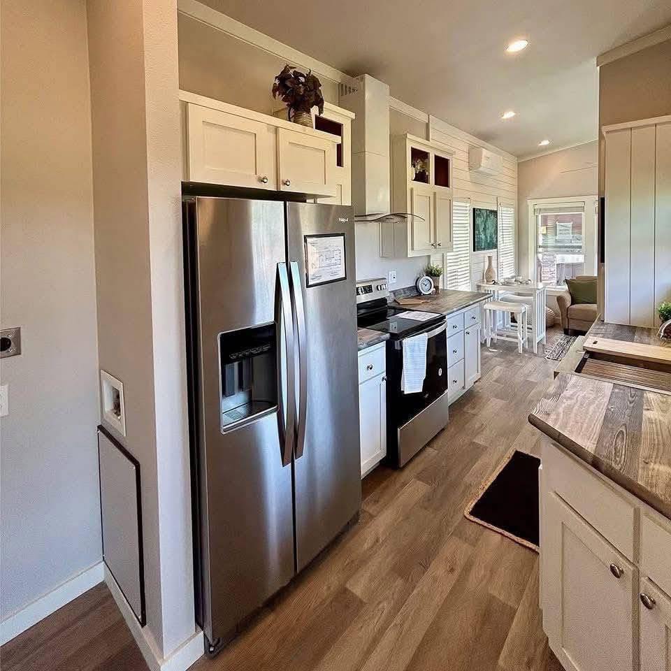 Modern kitchen with stainless steel fridge, white cabinets, and wood flooring. Bright dining area with white table and chairs leads to cozy living room.