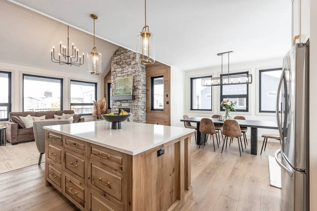 Modern open-concept kitchen and living area with a wooden island, pendant lights, a stone fireplace, dining table, and large windows. Cozy and elegant ambiance.