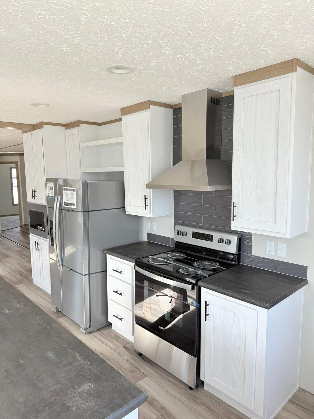 Modern kitchen with stainless steel appliances, white cabinets, gray backsplash, and wood-like flooring. Bright and minimalistic ambiance.
