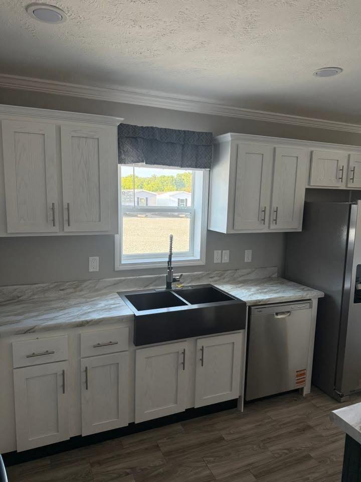 Modern kitchen with white cabinets, marble countertops, a large black sink under a window, and stainless steel appliances. Natural light filters in.