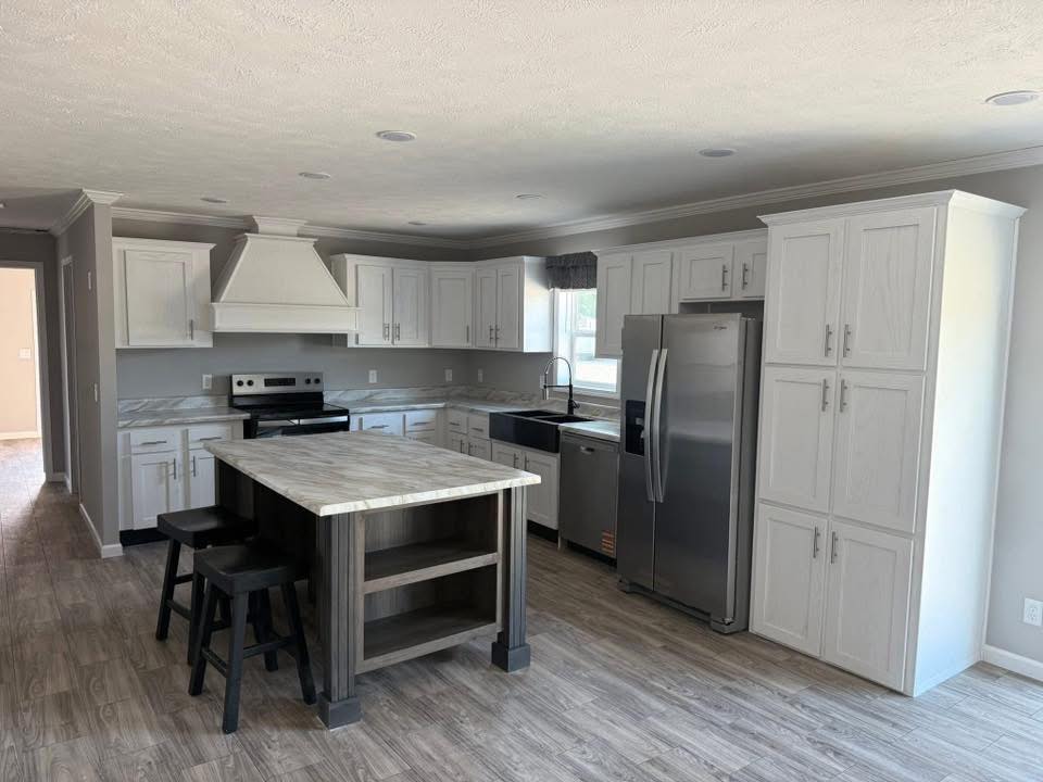 Spacious kitchen with light wood cabinets, stainless steel appliances, large central island with stools, and white marble countertops, conveying modern elegance.