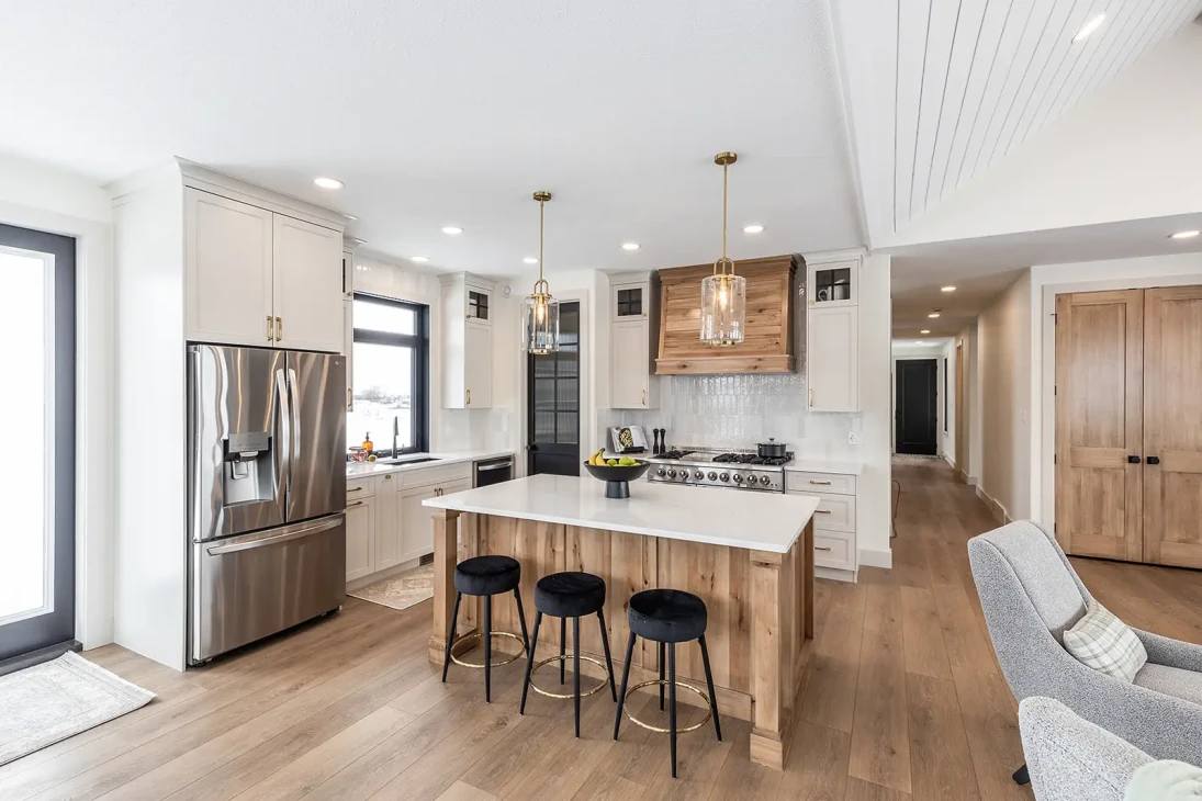 Modern kitchen with light wood flooring, white cabinetry, and stainless steel appliances. Central island with black stools and pendant lighting. Bright and inviting.