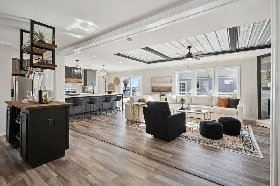 Modern open-plan living area with wood floors, featuring a kitchen with a black island, a dining table, and a cozy lounge with a white sectional sofa.