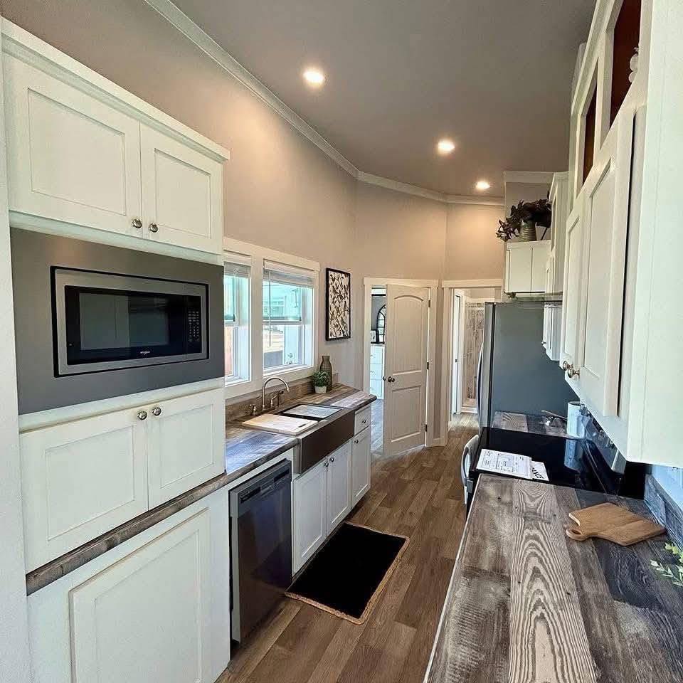 Compact modern kitchen with sleek white cabinets, wood-grain countertops, stainless steel appliances, and a gray wood floor. Bright, inviting, and tidy.