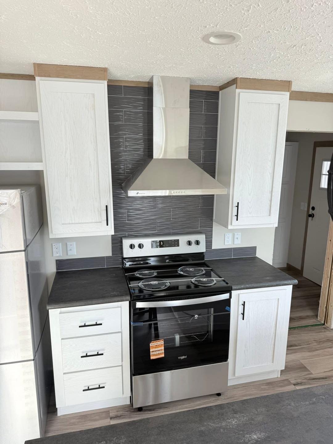Modern kitchen with white cabinets, a stainless steel stove, and a sleek range hood. Gray subway tiles form the backsplash, creating a clean, elegant look.
