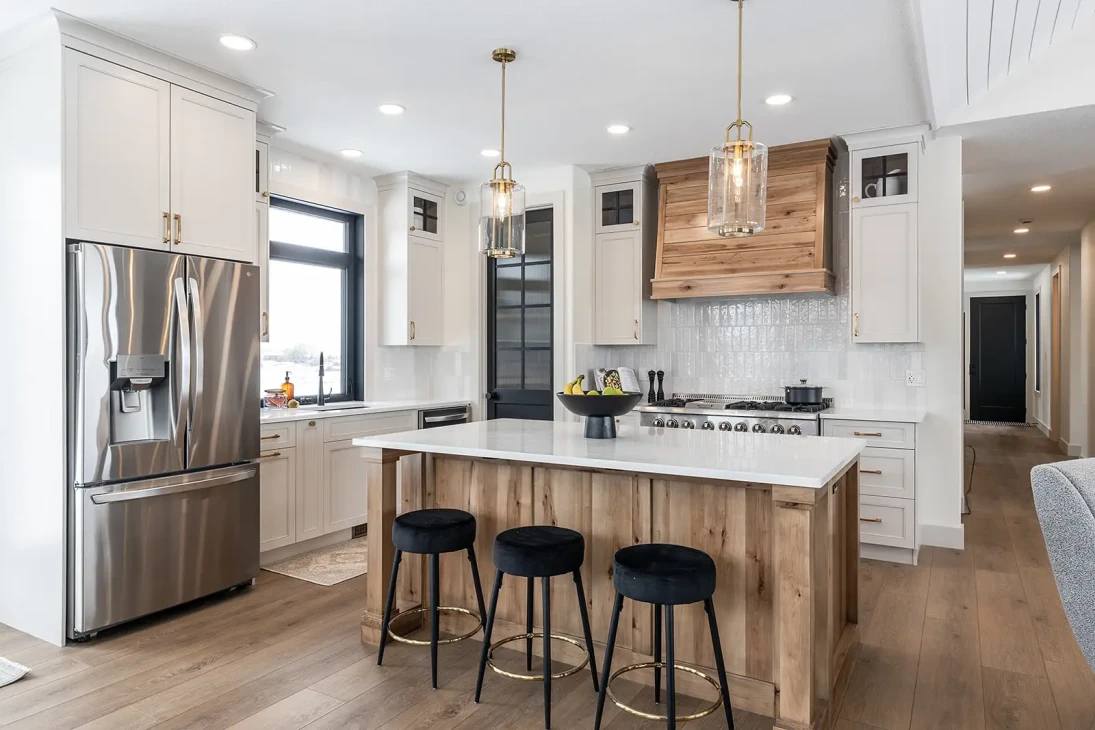 Bright, modern kitchen with wood accents. Features a central island with black stools, stainless steel appliances, and pendant lighting for a cozy ambiance.