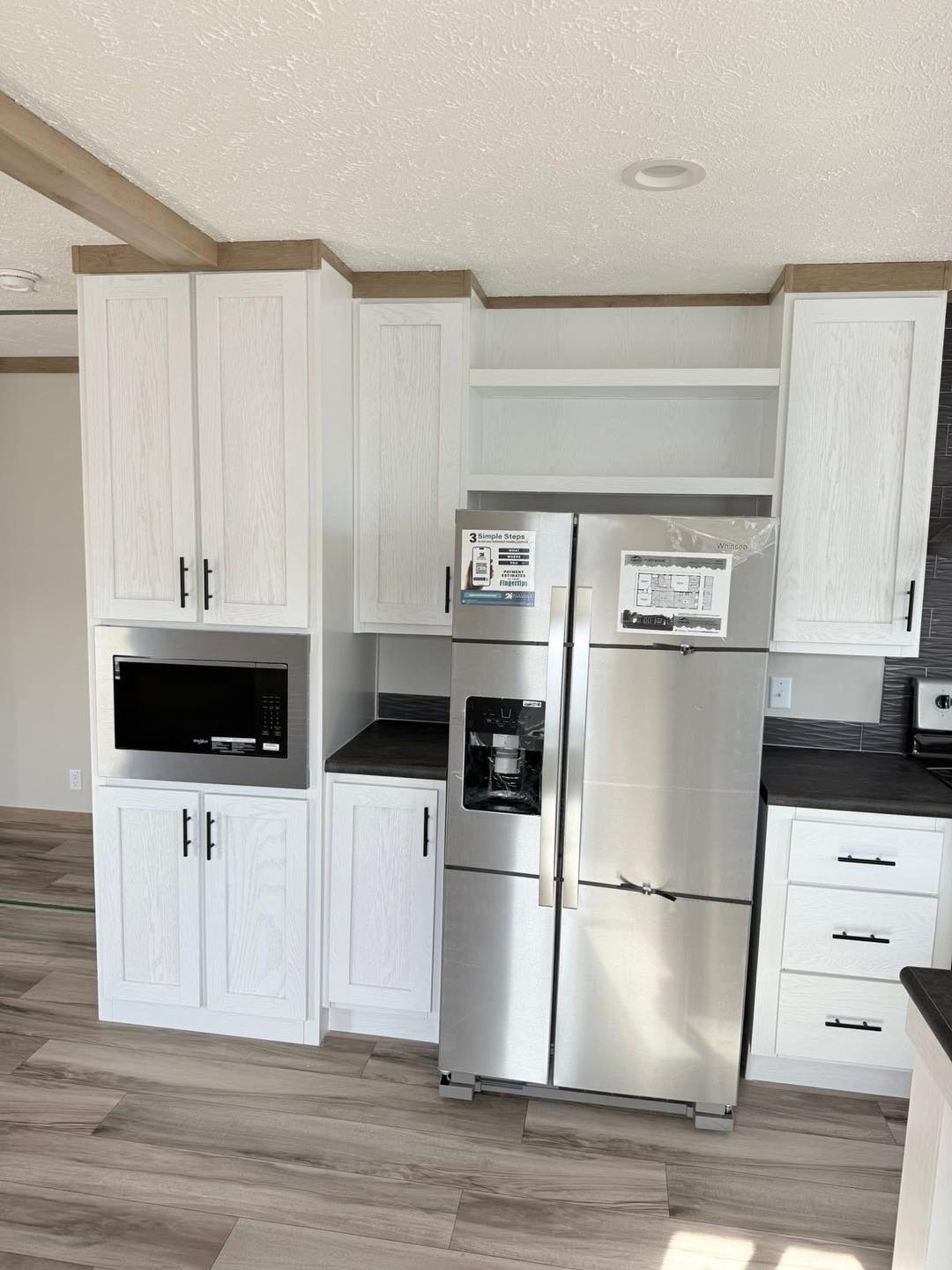 Modern kitchen with white cabinets, stainless steel refrigerator, and built-in microwave. Light wood flooring and dark countertops add contrast.