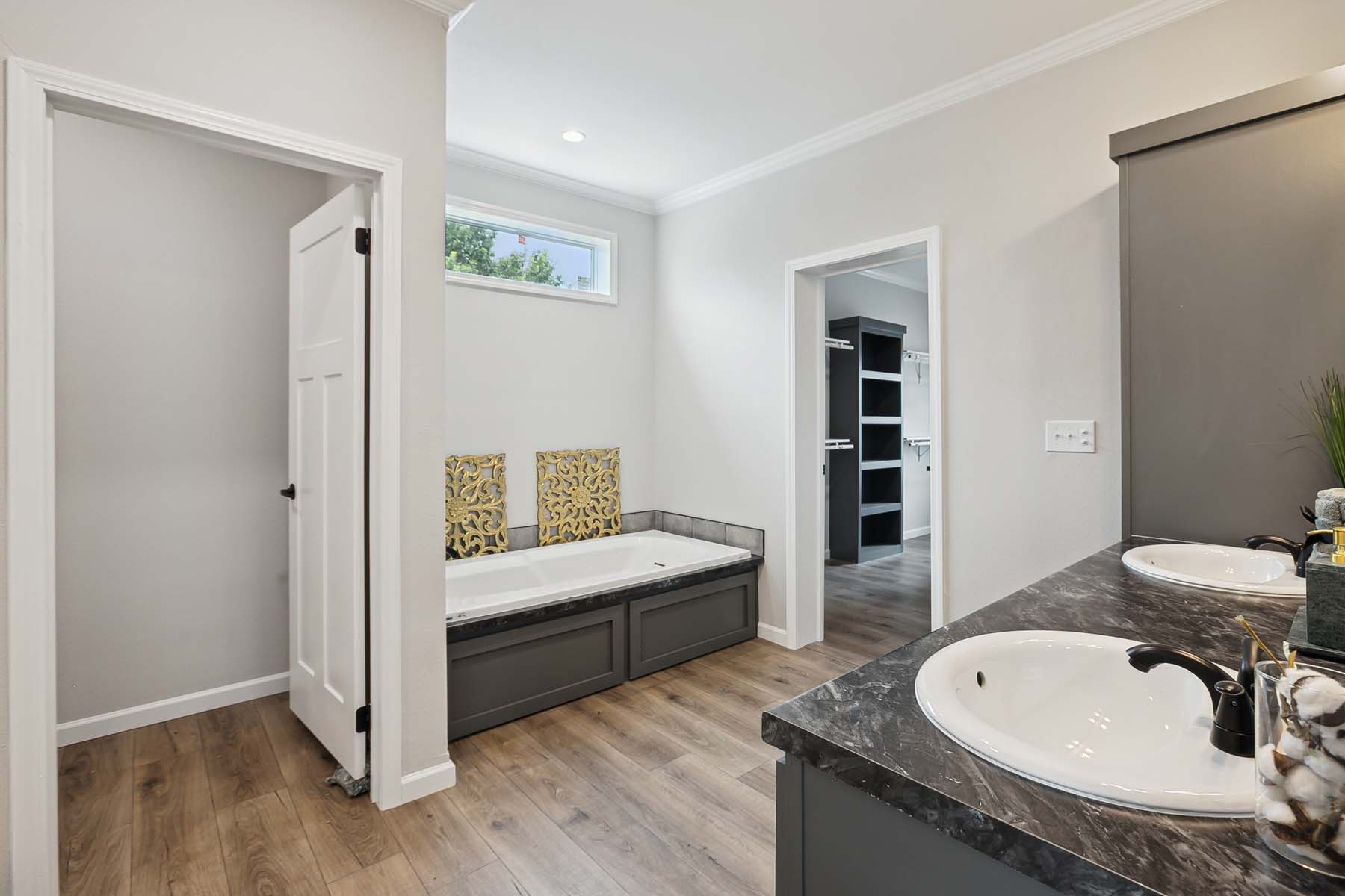 Spacious, modern bathroom with a marble counter, dual sinks, black fixtures, and a built-in tub. Light wood flooring and neutral walls enhance openness.