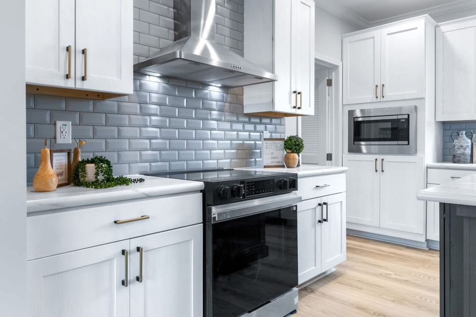 Bright, modern kitchen featuring white cabinets, a stainless steel range hood, and a sleek oven. Blue subway tiles add a stylish touch.