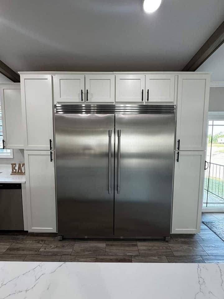 Modern kitchen with a large stainless steel double-door fridge, surrounded by white cabinets. Bright, clean, and minimalistic design.