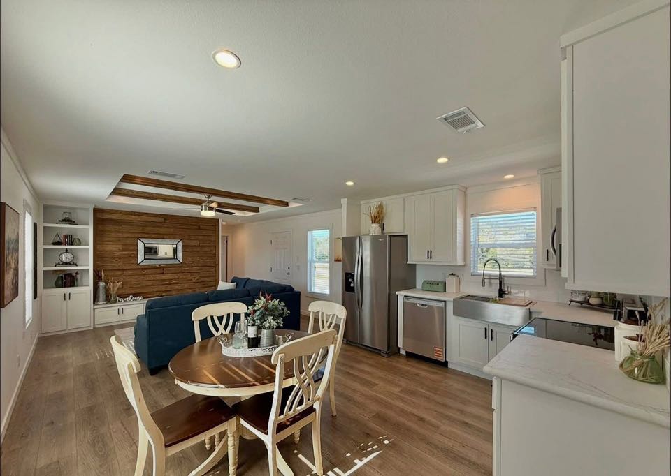 Bright, modern kitchen-living space with wood floors, white cabinets, stainless steel appliances, and a round dining table. Cozy, inviting ambiance.