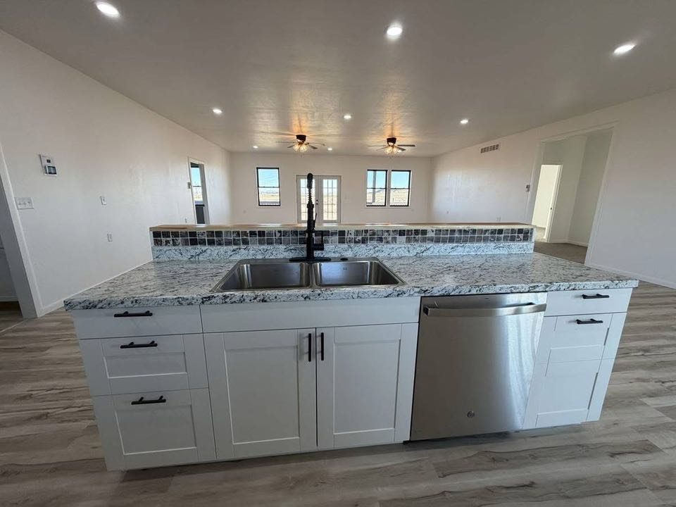 Spacious kitchen with white cabinets and granite countertops, featuring a central island with a dual sink. Open layout with light wood flooring.