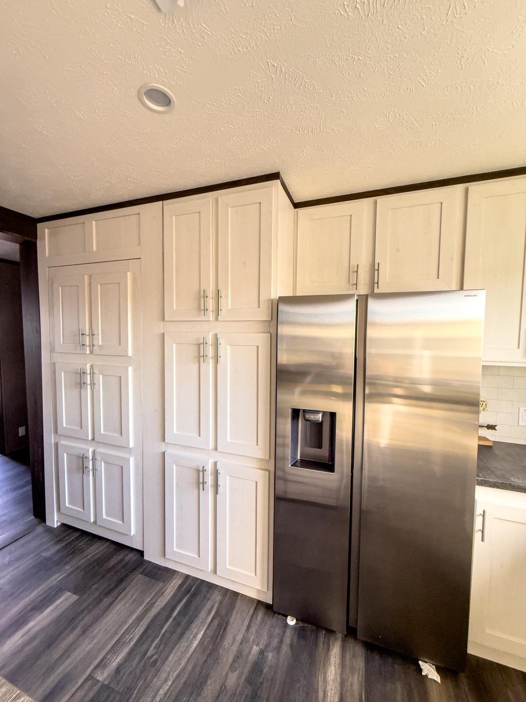 Kitchen with light wood cabinets and a stainless steel refrigerator. The flooring is dark wood, creating a modern and clean atmosphere.