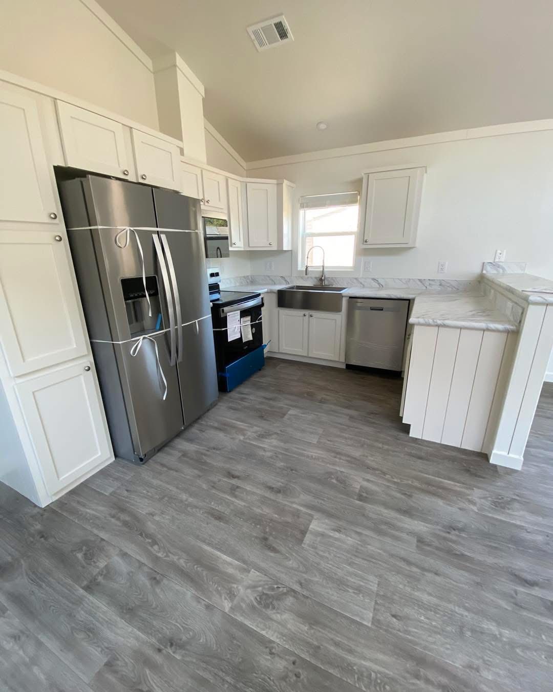 Modern kitchen with white cabinets, stainless steel refrigerator, and marble countertops. Gray wood floors add a sleek, contemporary feel.