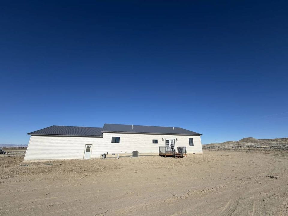 A single-story white house with a dark roof stands in an expansive, barren desert landscape under a clear blue sky, conveying isolation and tranquility.