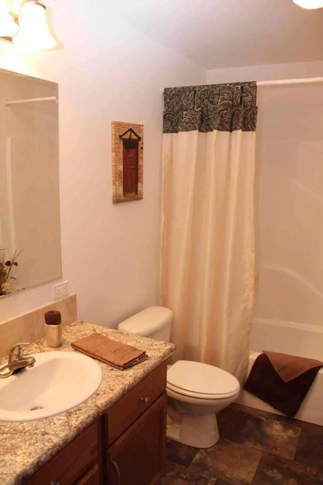 A modern bathroom with a granite countertop, sink, and wooden cabinets. Beige shower curtain, towel, and minimalistic decor create a warm, inviting atmosphere.